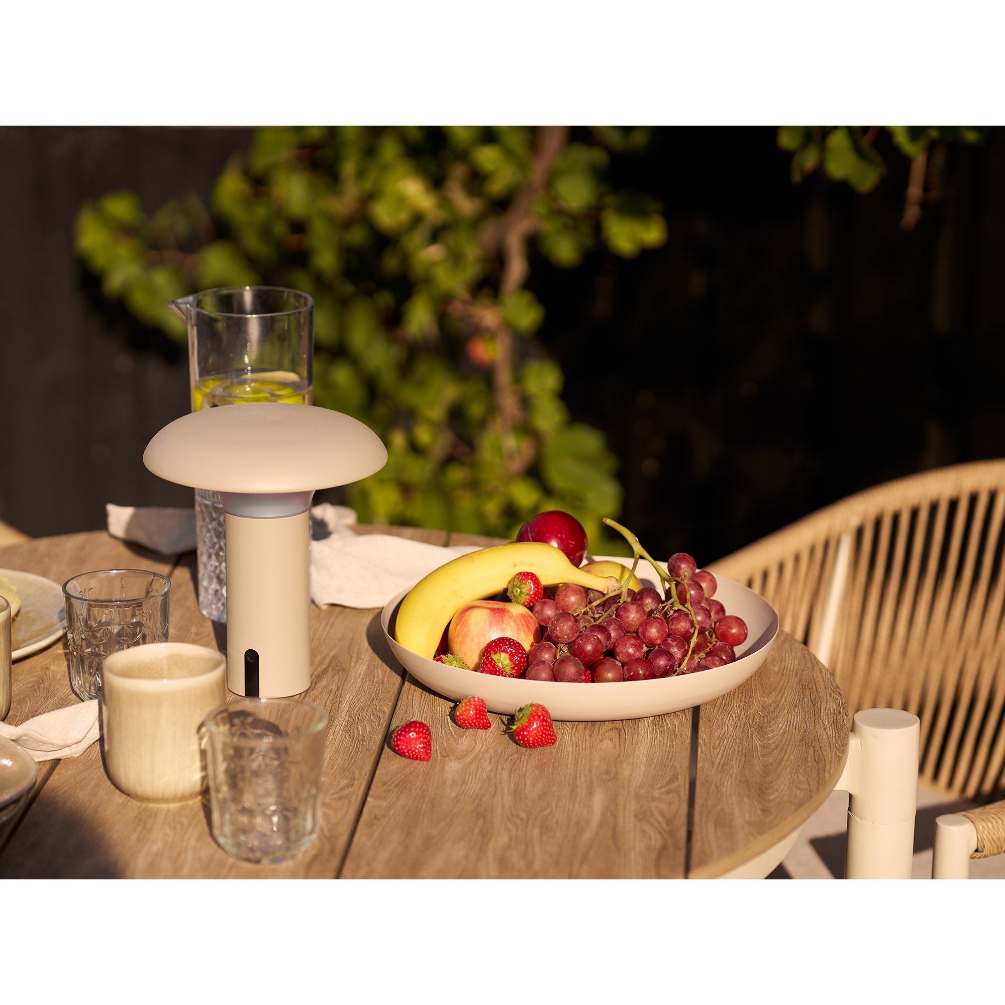 Lampe Ramsey beige sur table ronde terrasse bois avec salon de jardin tressé beige