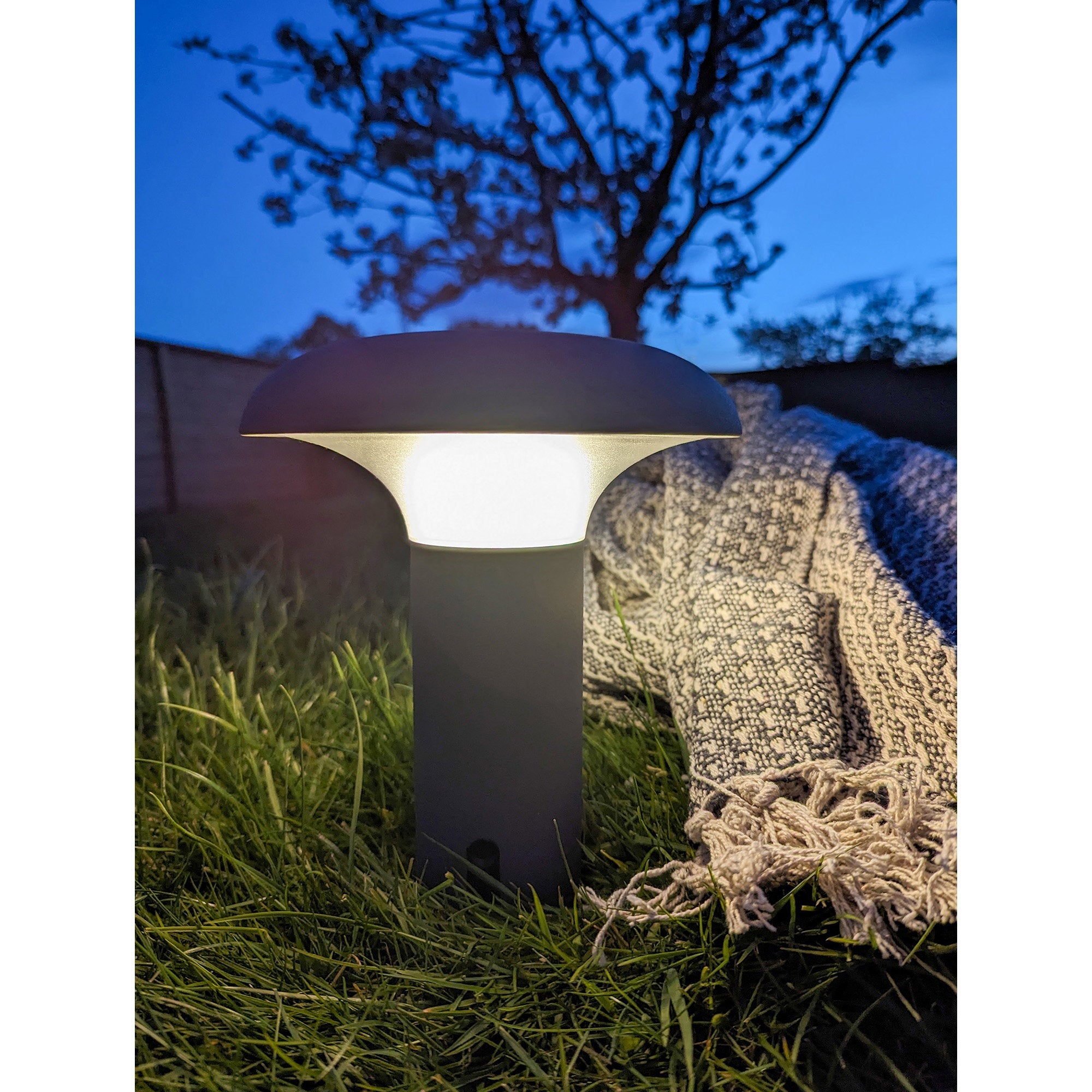 Lampe Ramsey LED gris allumée lumière chaude posée dans herbe jardin nuit étoilée