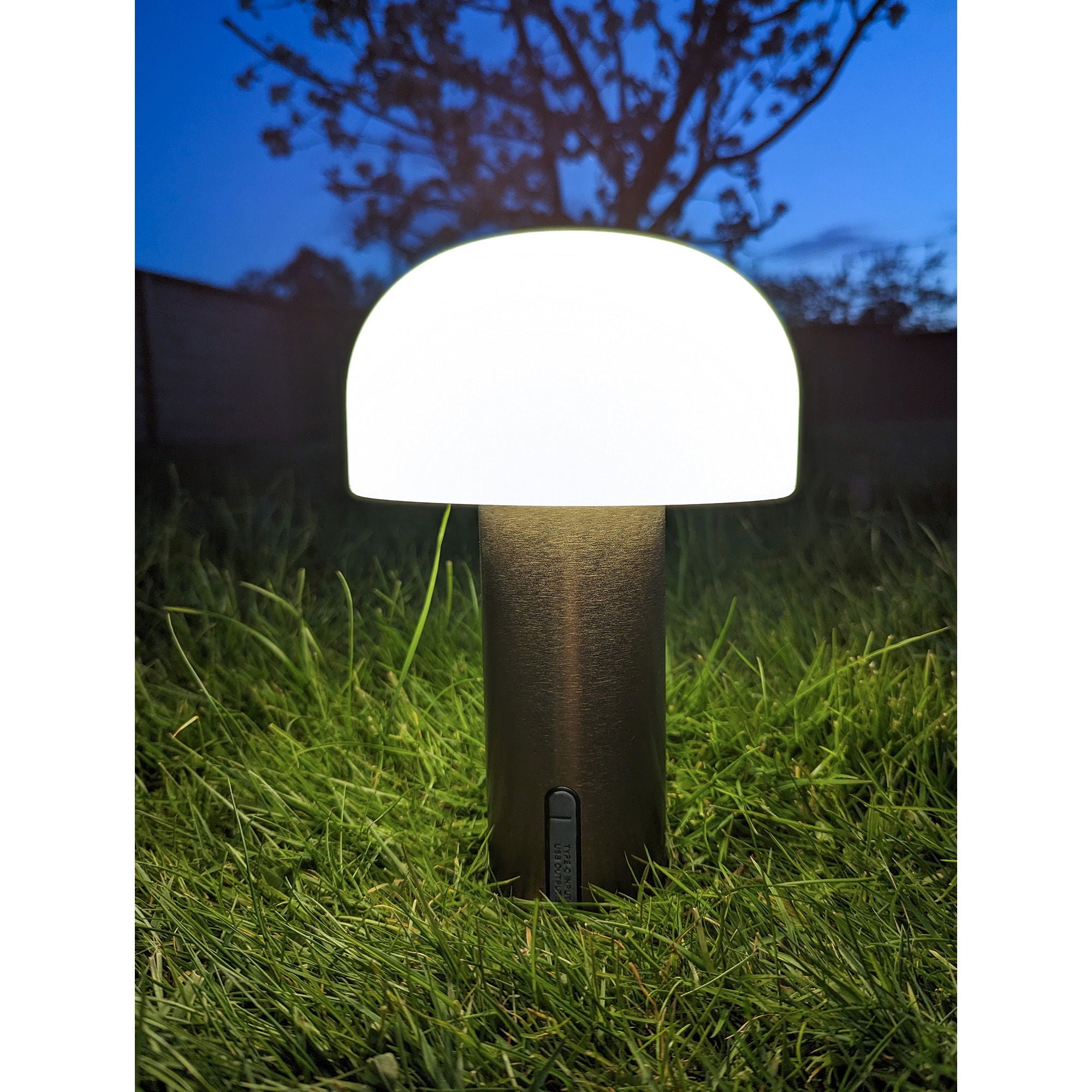 Lampe Soham LED cuivre allumée posée dans herbe jardin nuit lumière opaline chaude