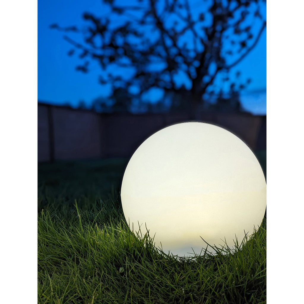 Lampe Lifton boule blanche allumée lumière chaude posée dans herbe jardin nuit