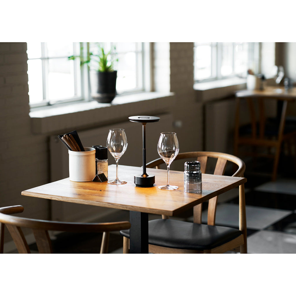 Lampe de table nomade Lyneham noire sur table restaurant bois ambiance dîner intime
