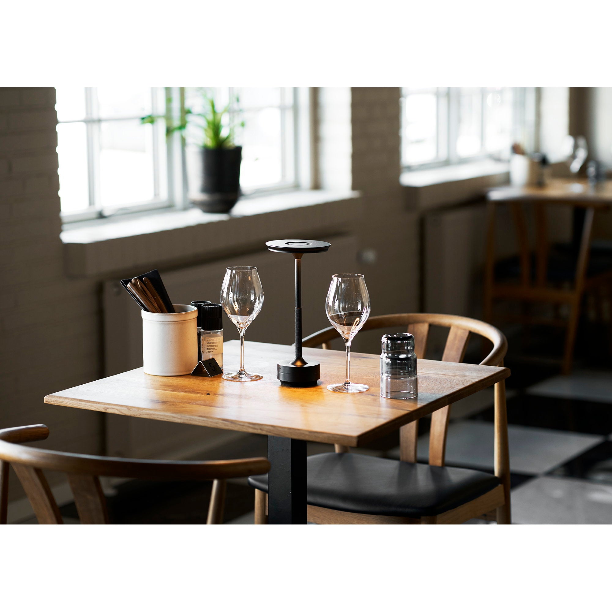 Lampe de table nomade Lyneham noire sur table restaurant bois ambiance dîner intime