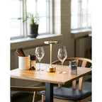 Lampe rechargeable Lyneham laiton doré allumée table bistrot bois ambiance dîner intime