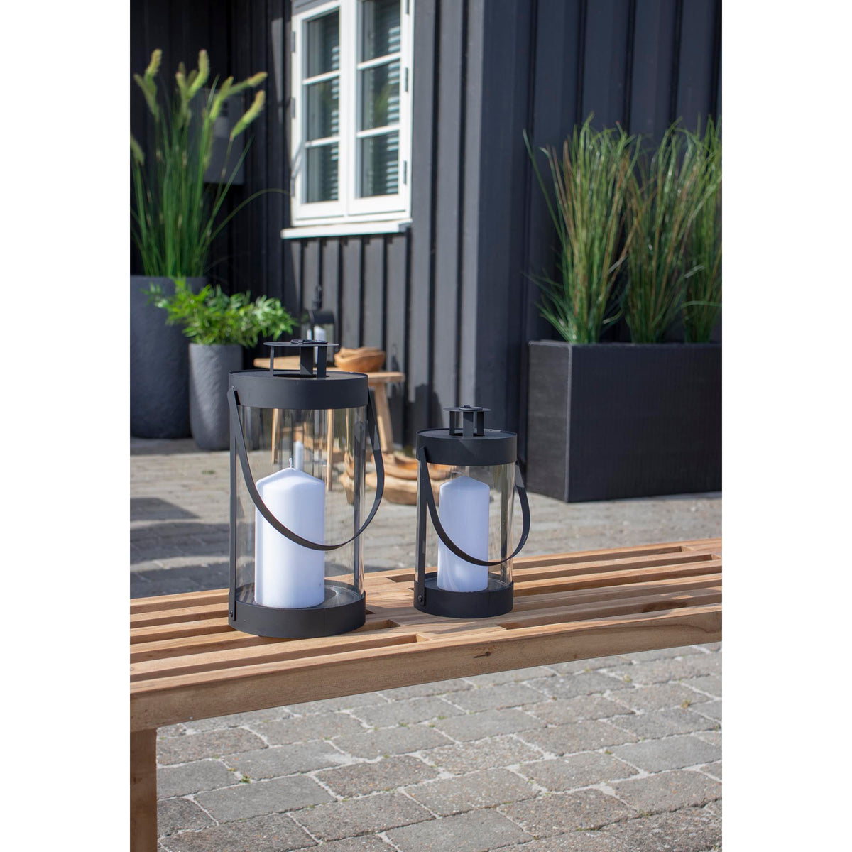 Lanternes Bondi avec bougies sur un banc à lattes en bois devant une façade noire