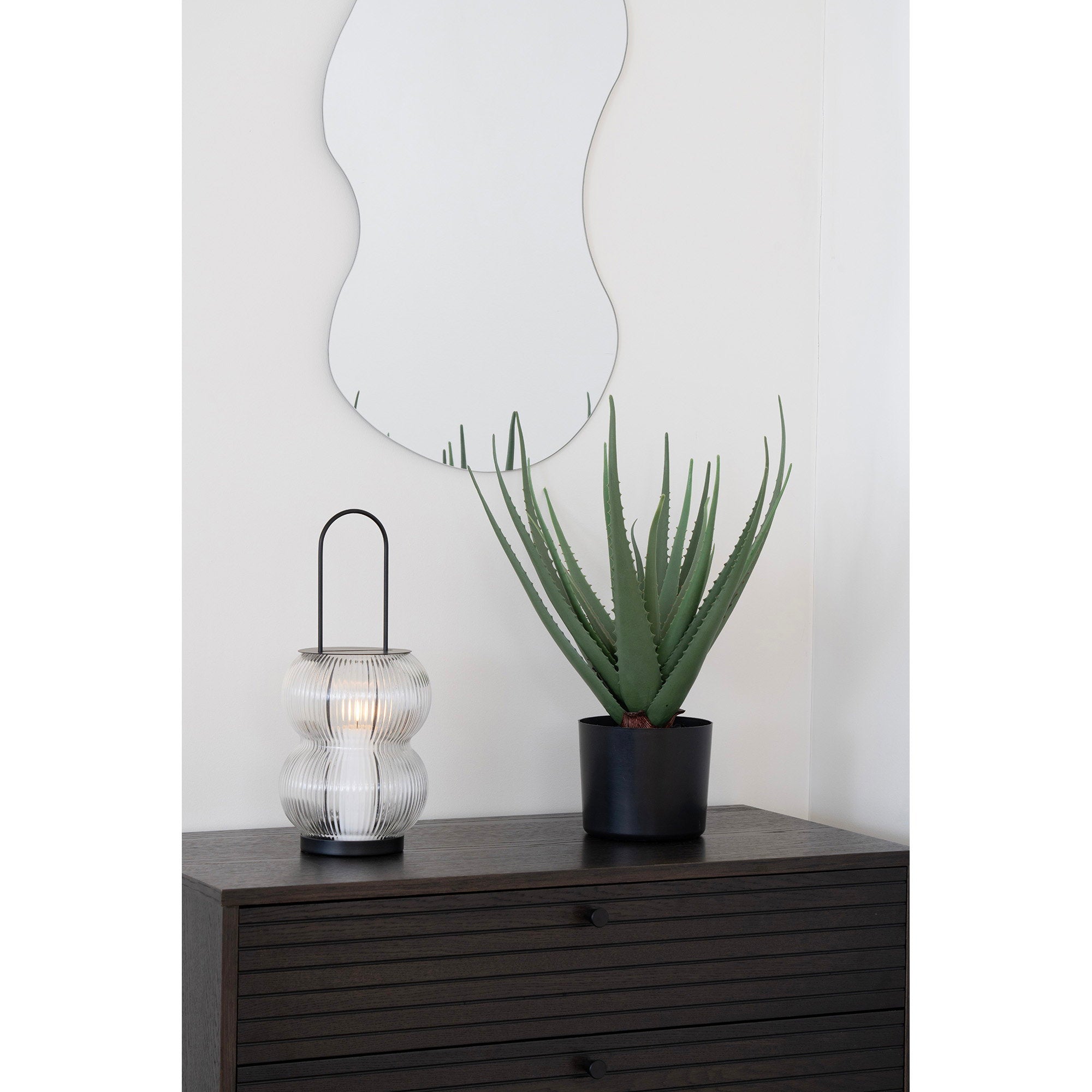 Lanterne Lucena bougie allumée sur commode bois sombre avec miroir organique mural