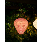 Lanterne Greatham rose poudré allumée de nuit sous une pergola couverte de lierre