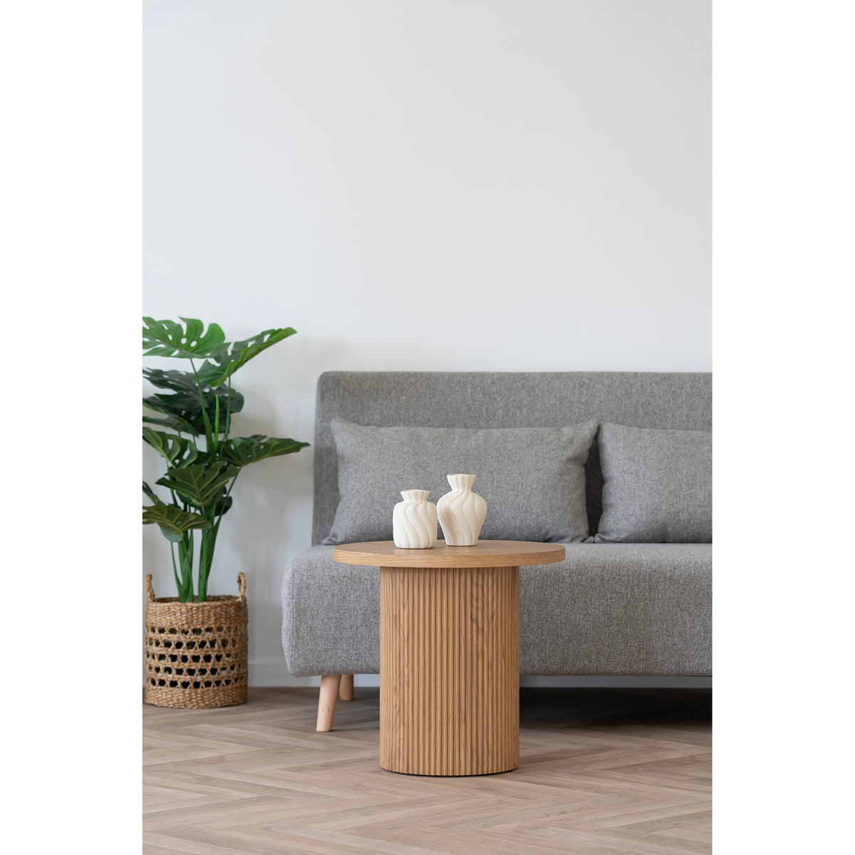 Les deux vases posés sur une table basse ronde en chêne cannelé devant un canapé gris
