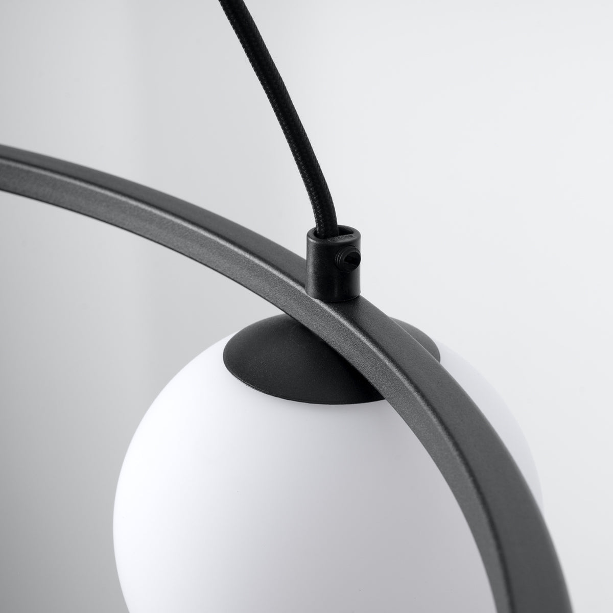 Détail du lustre Yoli 3 boule de verre opale fixée sous l'anneau d'acier noir et attache du câble