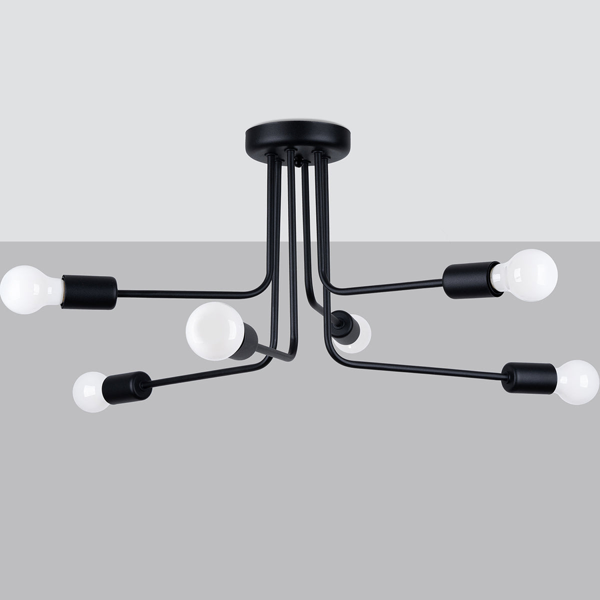 Lustre Norah à six branches noires vu sous un plafond blanc devant un fond gris