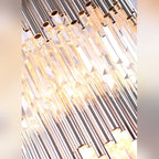 Détail des tubes en métal doré et des pampilles de verre facetté du lustre Vogue allumé
