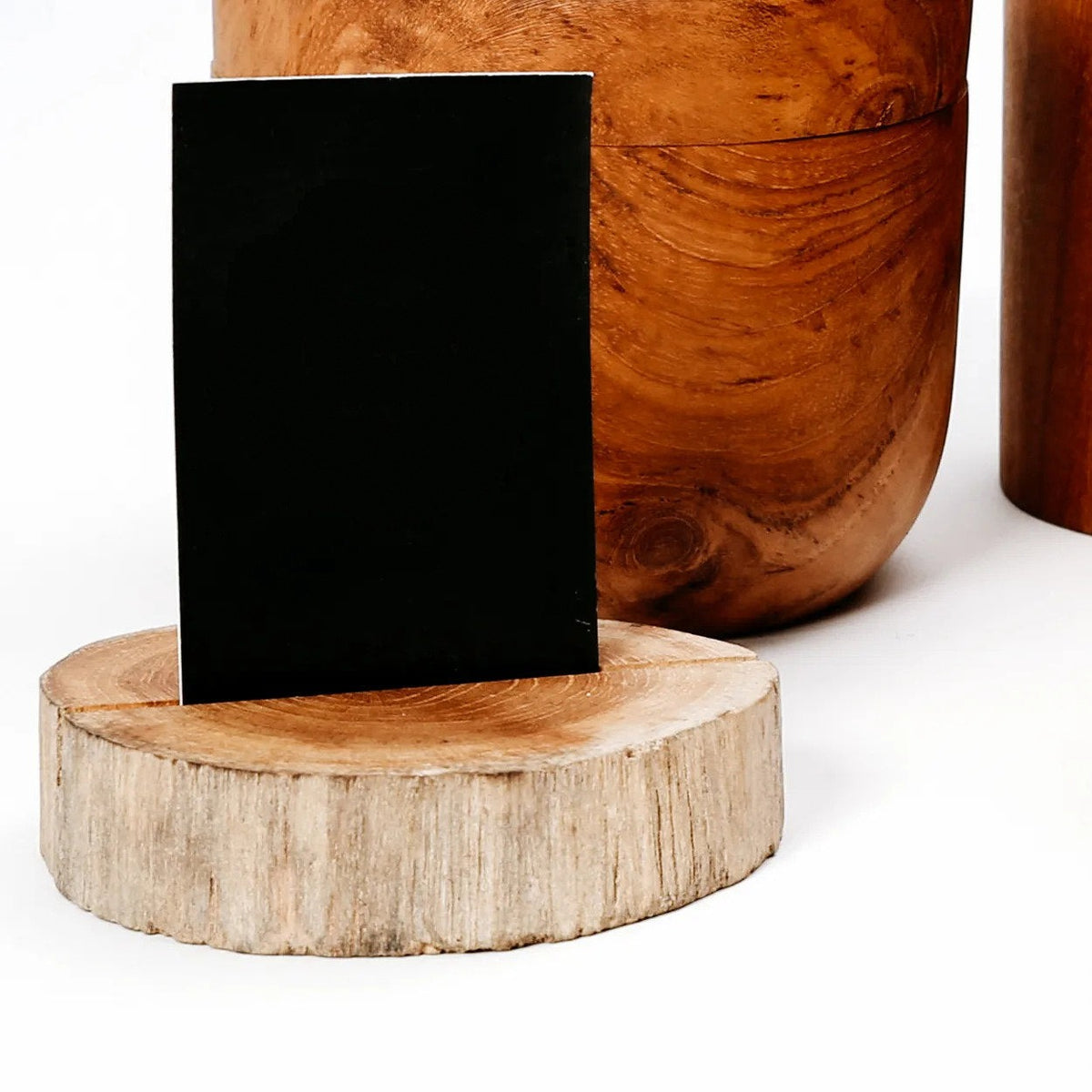 Marque-place en rondin de teck tenant un carton noir devant des pots en bois veiné