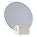 Miroir de table rond sans cadre vu de trois quarts glissé dans la fente d'un socle en travertin naturel