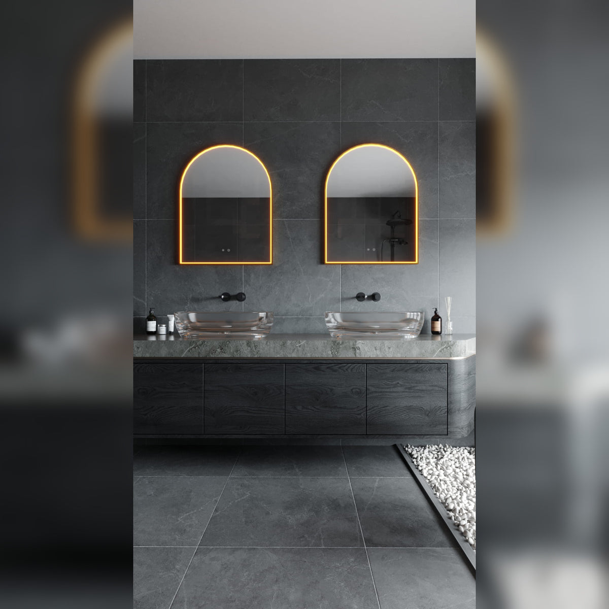Deux miroirs lumineux en arche allumés en lumière chaude au-dessus de deux vasques en verre posées sur un plan en pierre grise