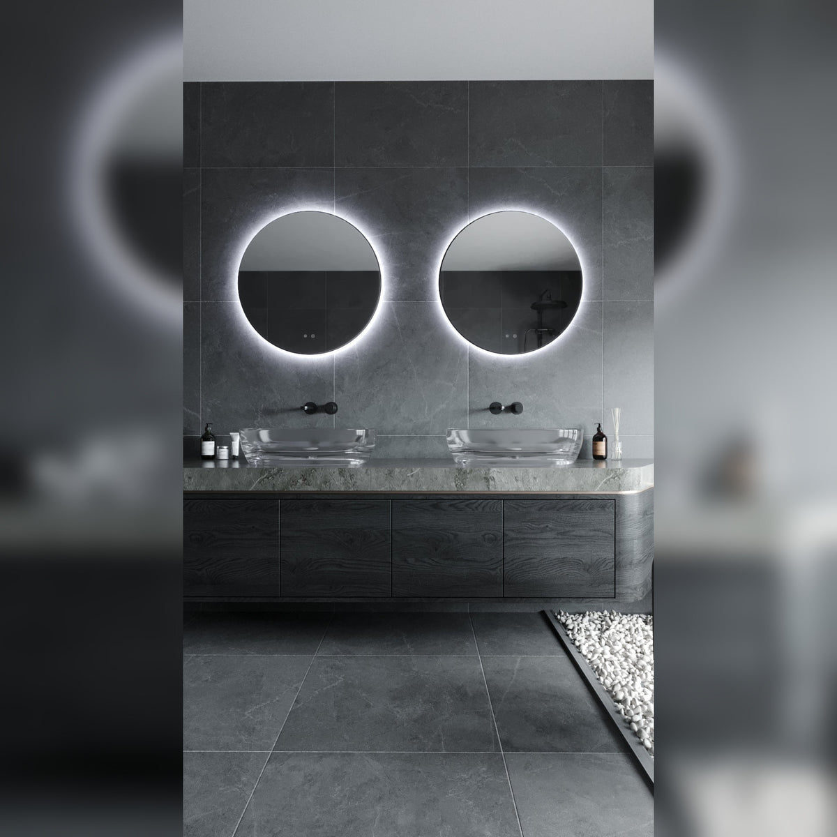 Deux miroirs lumineux ronds au halo blanc froid au-dessus d'une double vasque en verre dans une salle de bains en pierre grise
