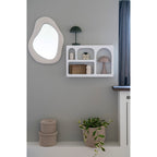 Miroir Bosa accroché sur un mur gris à côté d'une étagère murale blanche à niches arrondies