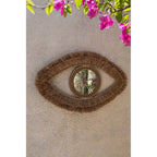 Miroir Raffia Eye en raphia accroché sur un mur en enduit beige sous des fleurs de bougainvillier