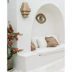 Miroir Raffia Eye dans une niche blanche en arc au-dessus d'une banquette près d'un bougainvillier en pot