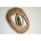 Miroir Raffia Eye vu de biais sur un mur blanc montrant le relief de sa double frange de raphia