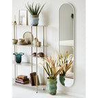 Miroir Hennetved accroché près d'une étagère en métal sable avec des vases en céramique et des herbes séchées