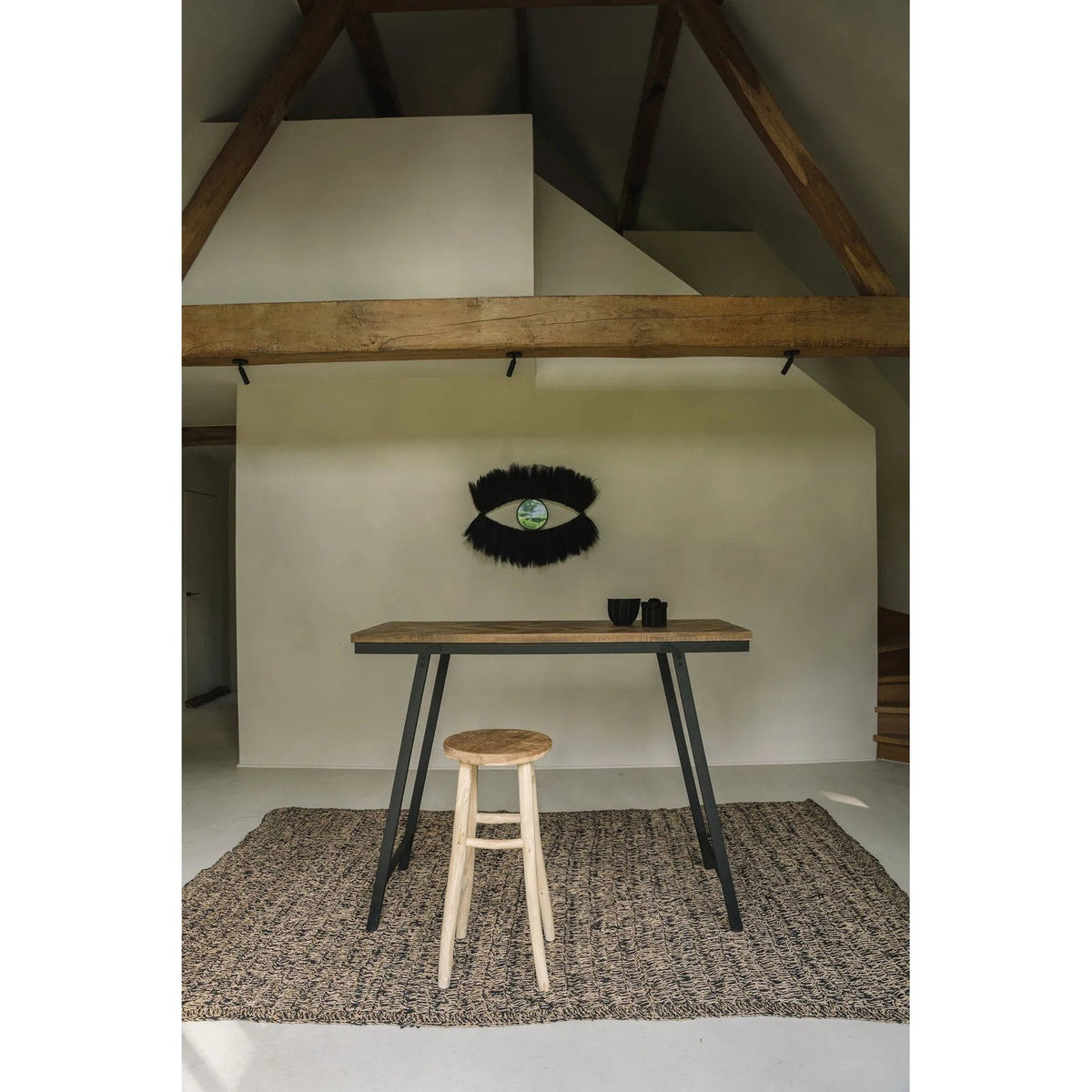 Miroir Black Eye sur un mur blanc sous une charpente en bois au-dessus d'une table haute
