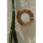 Miroir Palm Tree en raphia accroché sur un mur crépi blanc à côté d'un grand cactus