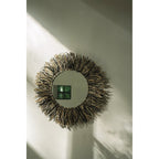 Miroir Raffia Fringe accroché sur un mur clair dans un rai de lumière avec son ombre portée