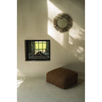 Miroir Raffia Fringe en raphia naturel et noir sur un mur blanc au-dessus d'un pouf près d'une cheminée à foyer vitré