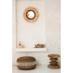 Miroir Mowgli au-dessus d'une tablette murale blanche avec un panier tressé et un pouf en fibre