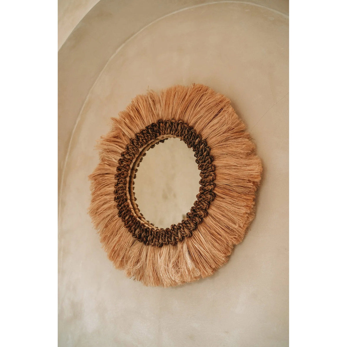 Miroir mural rond Mowgli accroché sur un mur en enduit clair vu de trois quarts