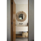 Salle d'eau vue par une porte en bois avec le miroir Pretty Blonde au-dessus du lavabo