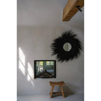 Miroir Simba en herbe rayung noire sur un mur blanc au-dessus d'une cheminée encastrée et d'un tabouret en bois