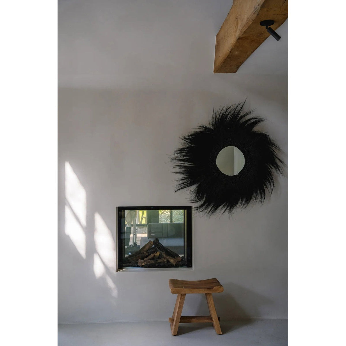 Miroir Simba en herbe rayung noire sur un mur blanc au-dessus d'une cheminée encastrée et d'un tabouret en bois