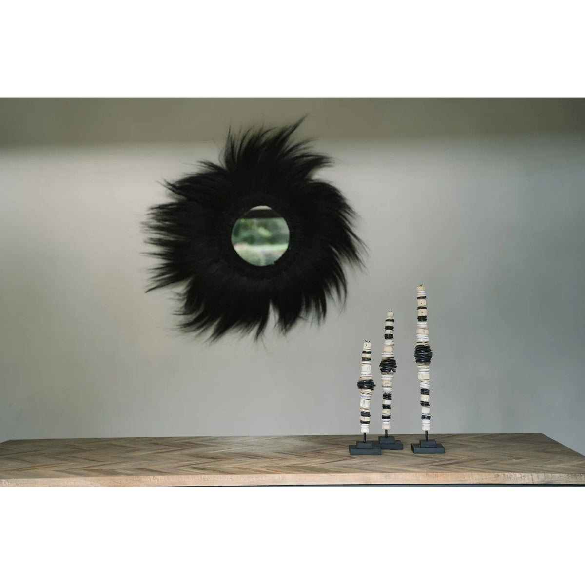 Miroir Simba en herbe rayung noire au-dessus d'une console en bois à chevrons avec trois sculptures sur socle