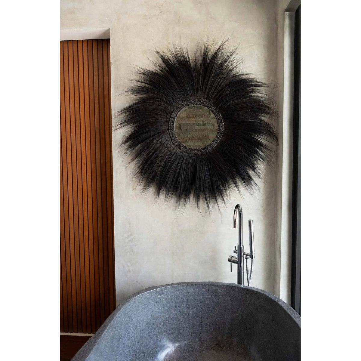 Miroir Simba en herbe rayung noire au-dessus d'une baignoire en pierre à côté d'une porte en lattes de bois