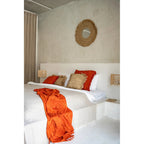 Miroir Yema vu de trois quarts au-dessus d'un lit avec coussins en raphia et plaid orange