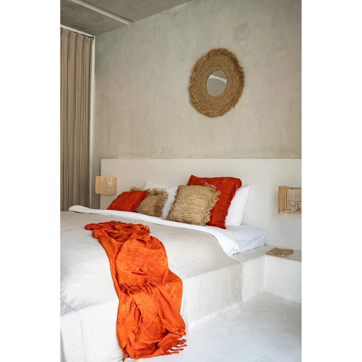 Miroir Yema vu de trois quarts au-dessus d'un lit avec coussins en raphia et plaid orange
