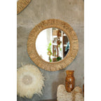 Miroir Tahiti sur un mur en béton brut au-dessus d'objets décoratifs en plumes et en coquillages