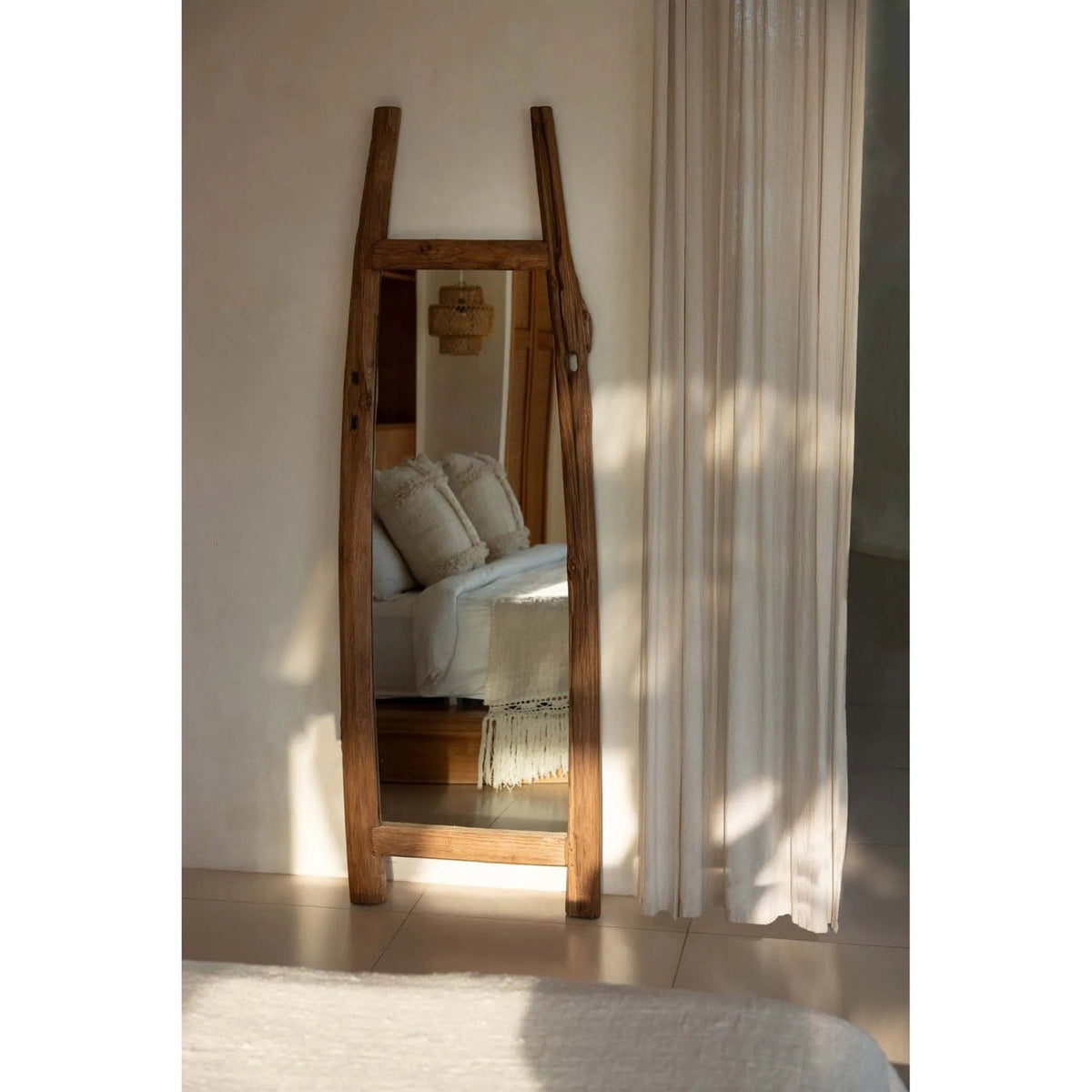 Miroir Fabulook adossé au mur d'une chambre près d'un rideau clair reflétant un lit