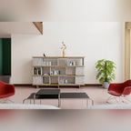 Salon avec une bibliothèque en modules Dice en béton et étagères plaquées chêne face à deux fauteuils rouges