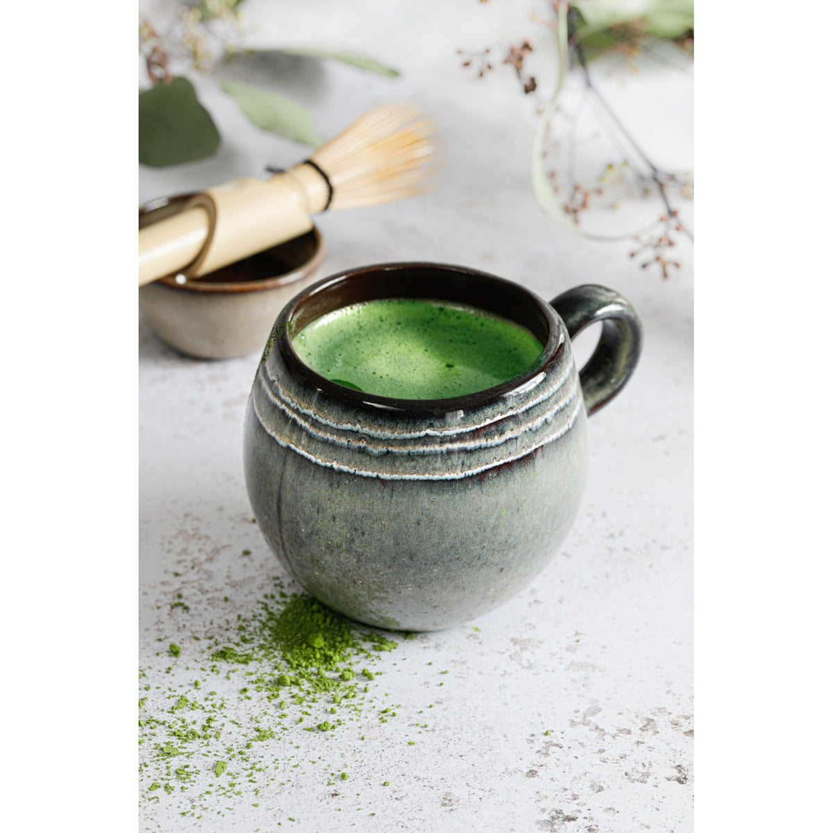 Mug boule Comporta rempli de matcha à côté d'un fouet en bambou et d'un bol assorti