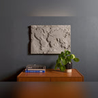 Œuvre murale The Gray Planet accrochée au-dessus d'un buffet en bois avec des livres et une plante