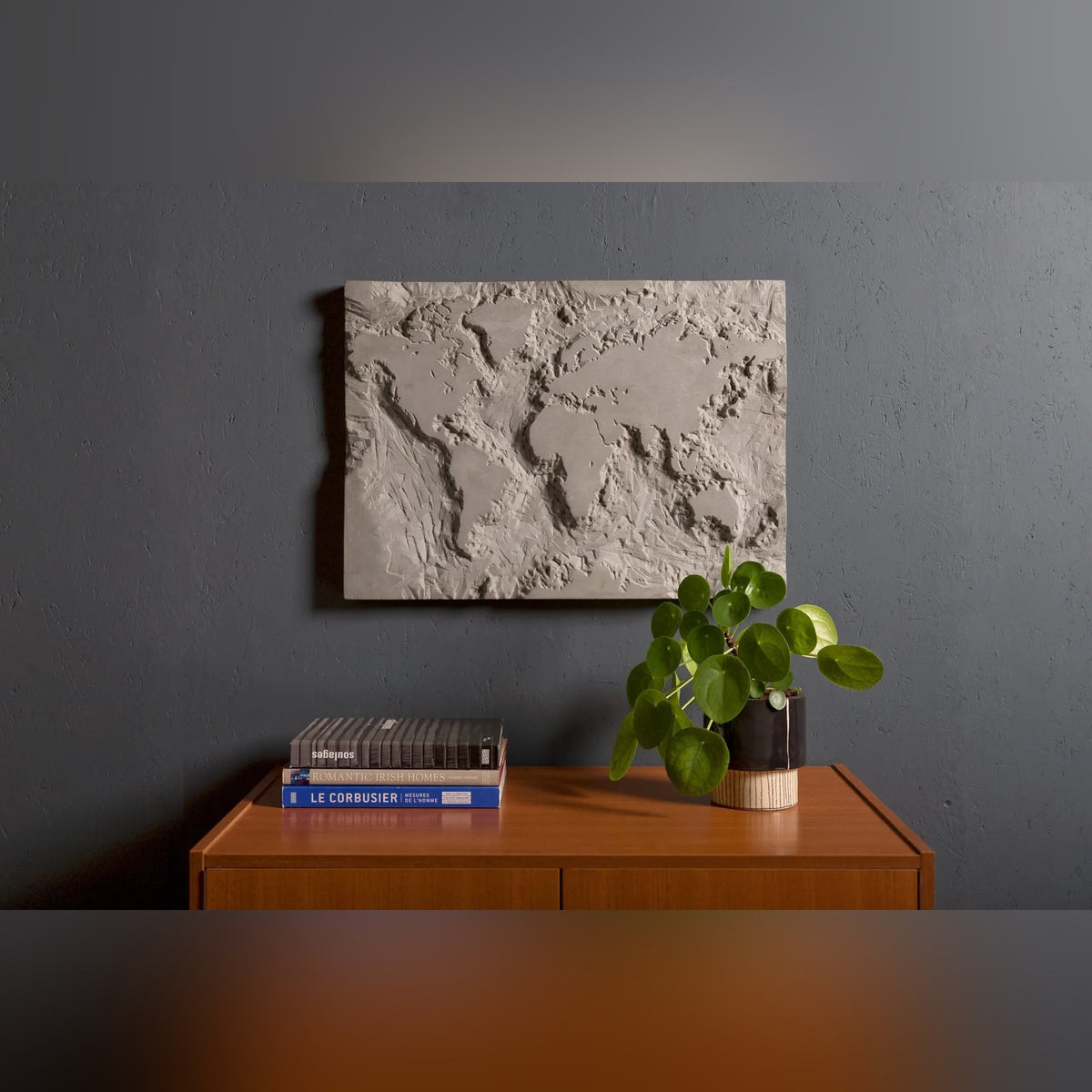 Œuvre murale The Gray Planet accrochée au-dessus d'un buffet en bois avec des livres et une plante
