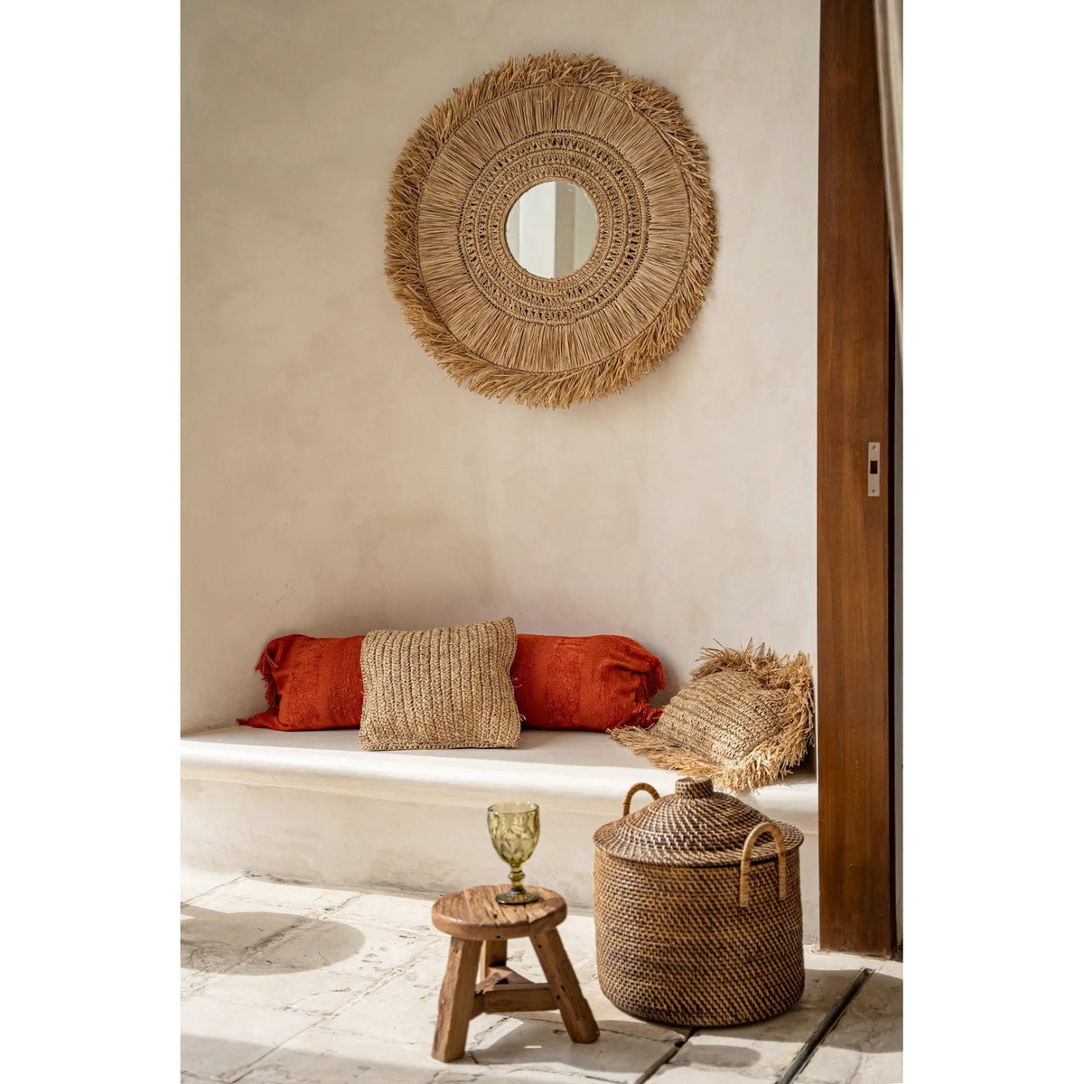 Panier Colonial en rotin posé au pied d'une banquette blanche à côté d'un petit tabouret en bois