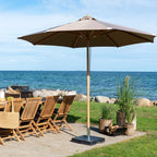 Parasol Austin taupe ouvert sur un pied noir près d'une table en teck et de chaises pliantes face à la mer