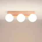 Plafonnier Bulbo 3 allumé au plafond avec ses trois globes lumineux sous la barre en bois clair