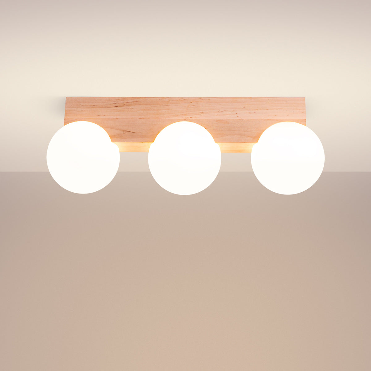 Plafonnier Bulbo 3 allumé au plafond avec ses trois globes lumineux sous la barre en bois clair