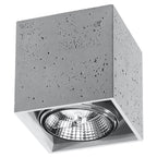 Plafonnier cube Valde en béton gris vu de trois quarts avec son ouverture carrée et son ampoule à réflecteur