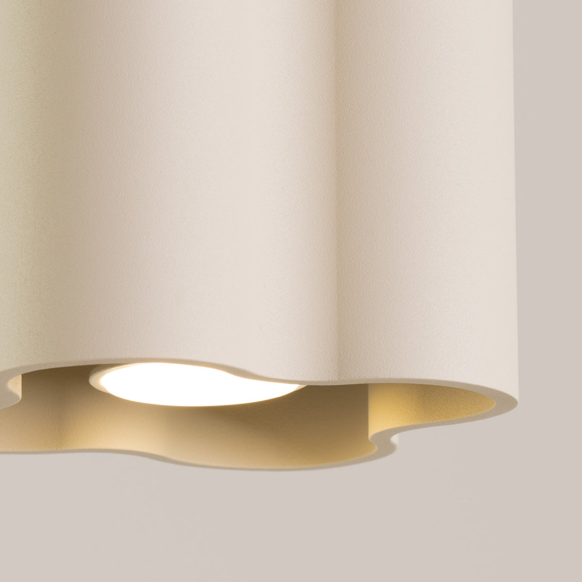 Détail du bord ondulé et de l’ampoule allumée du plafonnier Ovio laque beige