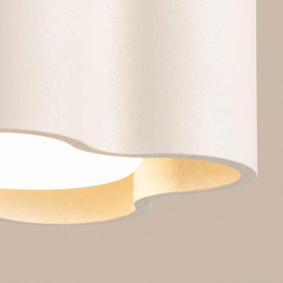 Détail du bord ondulé et de l'ampoule allumée du plafonnier Ovio laque beige