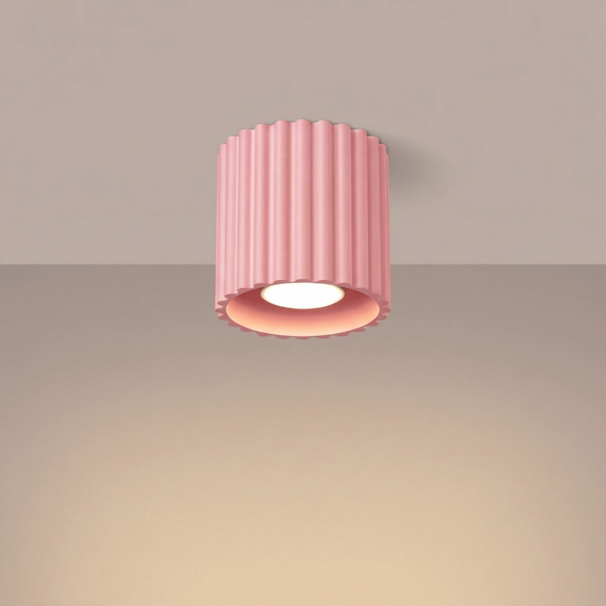 Plafonnier spot Aura 1 en laque rose allumé au plafond avec sa lumière dirigée vers le bas